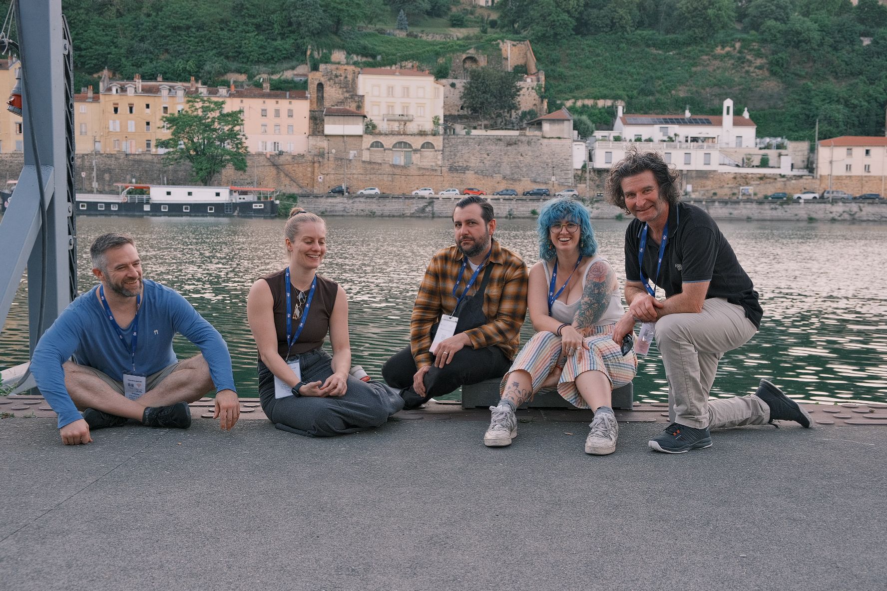 Five people sit by a river and laugh with each other.